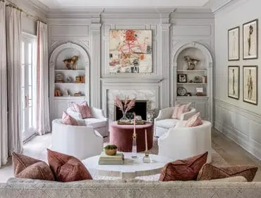 Gray living room with white swivel chairs, pink pillows, and abstract art above fireplace.