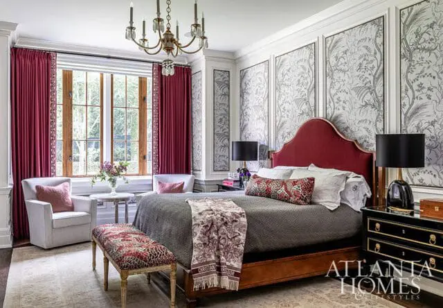 Bedroom with a red upholstered headboard, gray bedding, and patterned wallpaper. Burgundy curtains frame a large window, and a black lacquered nightstand sits beside the bed.