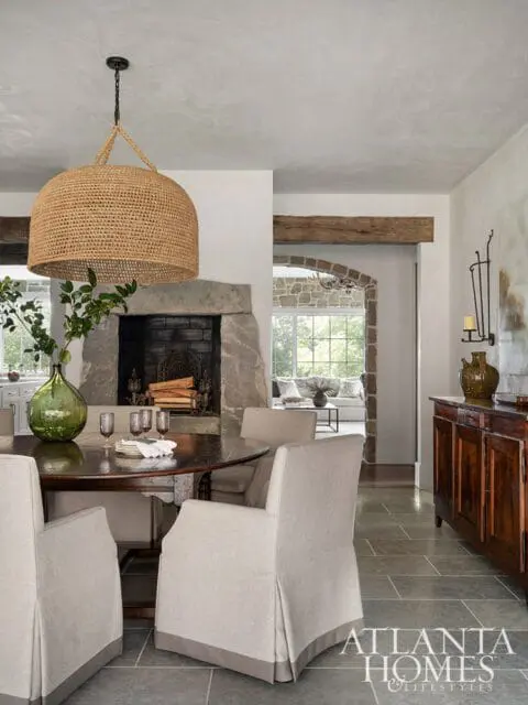 Dining room with stone fireplace, round wooden table with upholstered chairs, and a large woven pendant light.