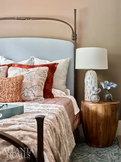 Bedroom with a light blue upholstered headboard, metal bed frame, and a bedside table with a white textured lamp and wooden stool.