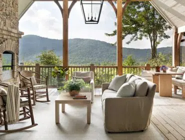 Covered porch with stone fireplace, rocking chairs, sofa, coffee table, and dining set overlooking