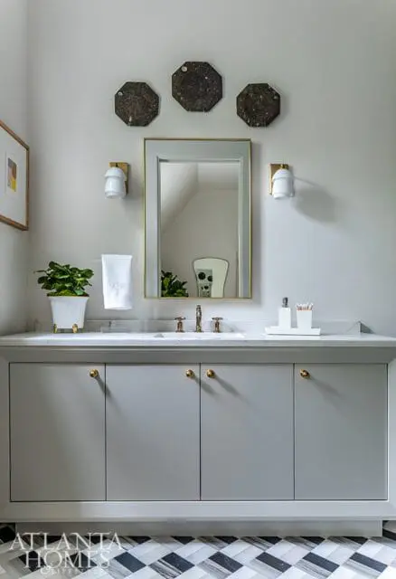 Gray bathroom vanity with marble countertop, brass hardware, and a gold-framed mirror. Octagonal wall art hangs above the mirror.