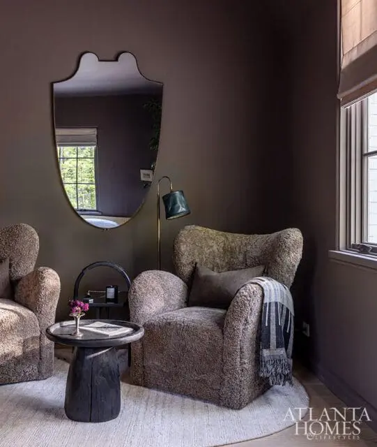 Dark brown bedroom with two plush armchairs, a dark wood side table, a decorative mirror, and a floor lamp.