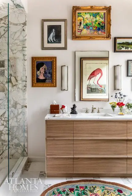 Bathroom with marble shower, wood vanity with white countertop, and gallery wall featuring artwork of a dog, a woman, a flamingo, and a landscape.