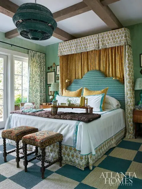 Bedroom with teal and gold patterned canopy bed, green walls, wood beam ceiling, and a large woven pendant light.