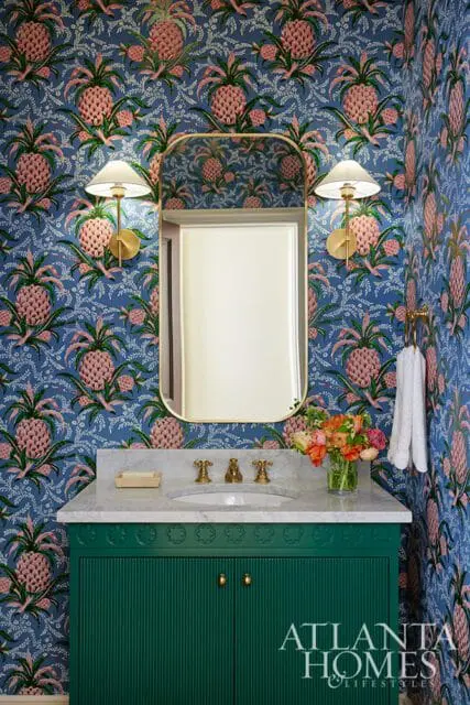 Powder room with blue pineapple wallpaper, a green fluted vanity, marble countertop, brass fixtures, and a gold-framed mirror.