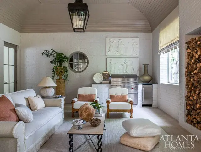 Covered porch with white brick walls, vaulted ceiling, and a built-in grill station. Furnishings include a sofa, armchairs, and a coffee table.