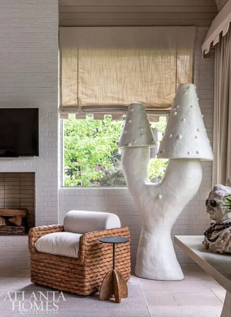 Living room with white brick fireplace, woven armchair with white cushions, and a large white mushroom-shaped sculpture.