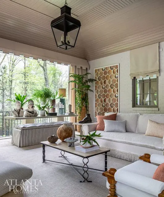 Covered porch with white brick walls, a large black lantern, and a sofa with light-colored upholstery and fringe trim.