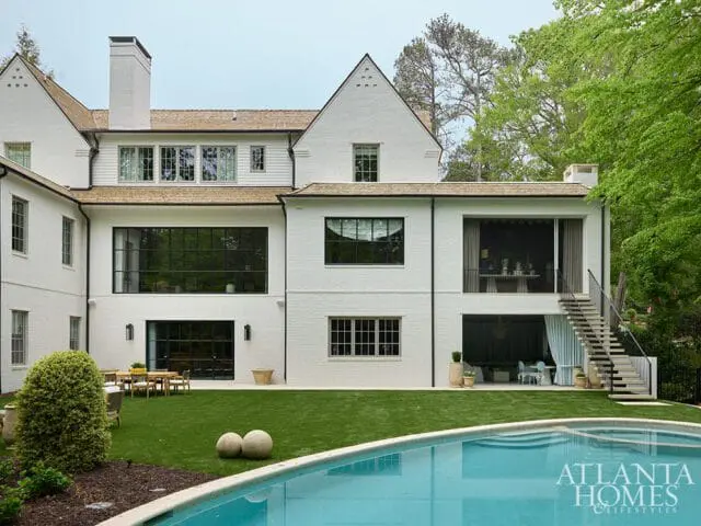 Modern white brick home with large black-framed windows, a shingled roof, and an outdoor swimming pool.