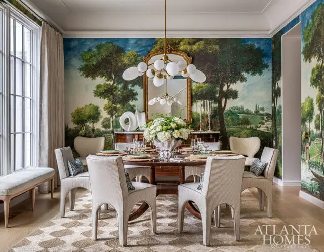 Dining room with a large mural of a landscape scene, a round wooden table set for dinner, striped chairs, and a modern chandelier.