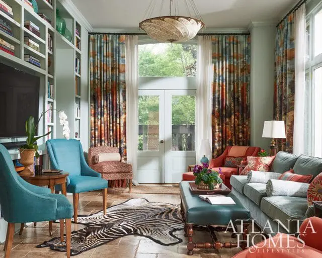 Living room with teal chairs, patterned curtains, zebra rug, and a teal ottoman. Built-in bookshelves line the wall.