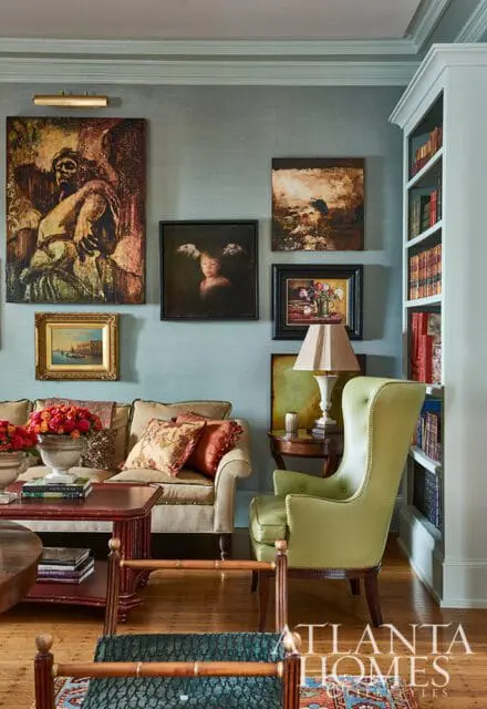 Living room with a light blue textured wallpaper, a tan sofa with patterned pillows, a lime green wingback chair, and a built-in bookshelf filled with books.