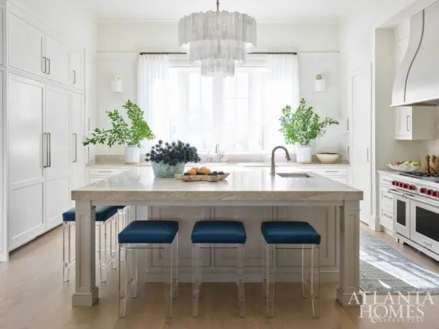 White kitchen with a large marble island, blue bar stools, white cabinetry, and a professional range.