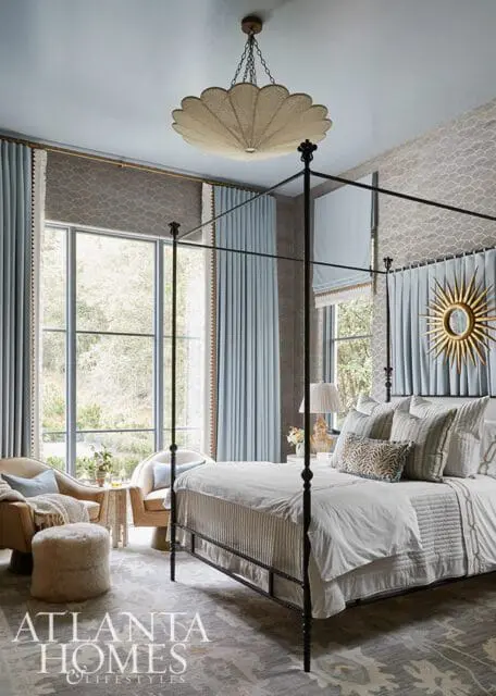 Bedroom with a black metal canopy bed, light blue drapes, patterned wallpaper, and a large window overlooking trees.