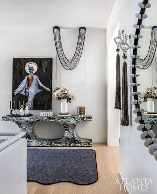 Foyer with a marble console table, abstract art, and cascading chain chandeliers. A dark rug lies on the wood floor.
