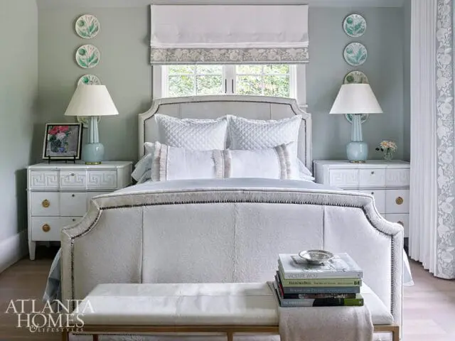 Serene bedroom with a light blue upholstered headboard, white quilted bedding, and matching bedside tables. Decorative plates adorn the pale blue walls above the tables.