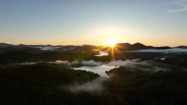 Sunrise over misty mountains and lakes, with sunbeams radiating from the horizon and illuminating the landscape.