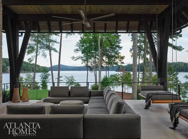 Covered outdoor living space with a large sectional sofa, hanging daybed, and a view of a lake and trees.