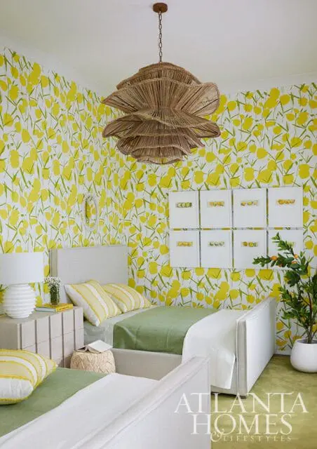 Bedroom with yellow floral wallpaper, two twin beds with green bedding, a rattan chandelier, and framed artwork.