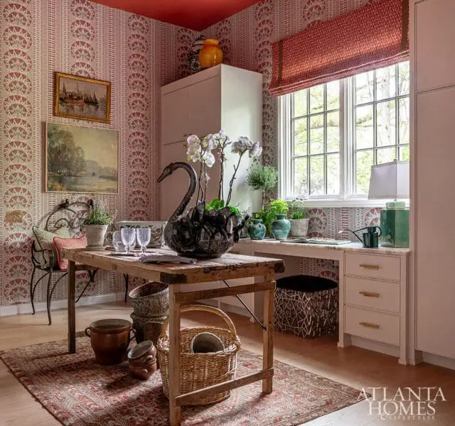 Mudroom with red and white patterned wallpaper, a wooden table with a black swan planter, and a desk with a window overlooking trees.