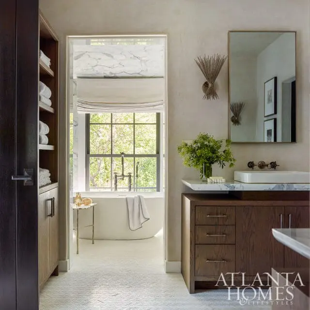 Luxury bathroom with a freestanding tub visible through a doorway, a dark wood vanity with a marble countertop and white sink, and a large mirror with a decorative sconce.