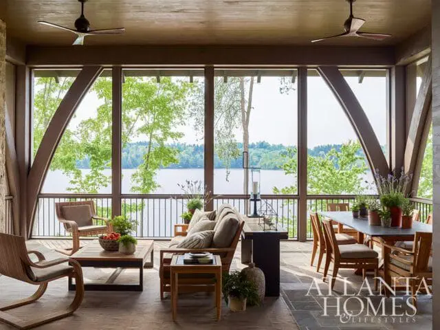 Screened porch with wooden beams, ceiling fans, and lake view. Furnished with a sofa, armchairs, coffee table, and dining set.