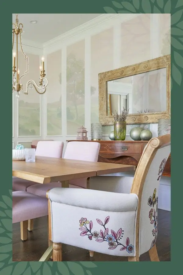 Dining room with a light wood table, pink upholstered chairs, and a buffet with a gold ornate mirror above. The walls feature a scenic mural.