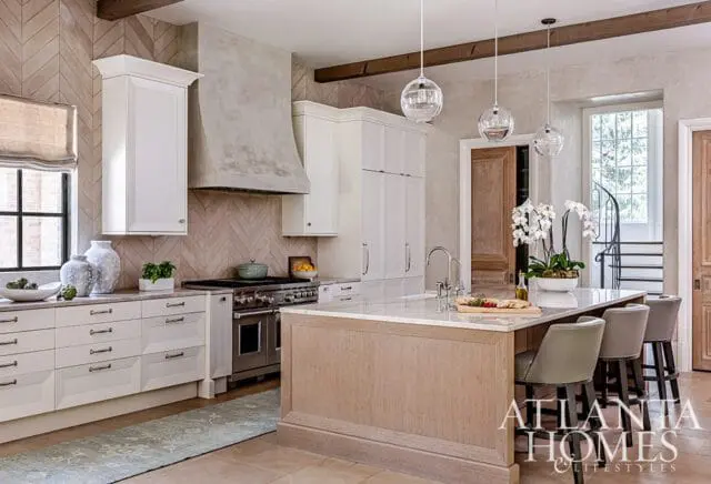 Kitchen with white cabinetry, a concrete range hood, herringbone tile backsplash, and a light wood island with a marble countertop.