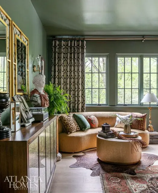 Green living room with a curved mustard sofa, patterned curtains, a wooden credenza with mirrored doors, and a bust sculpture.
