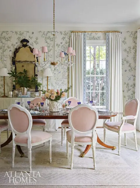 Dining room with pink velvet chairs, floral wallpaper, and a crystal chandelier.