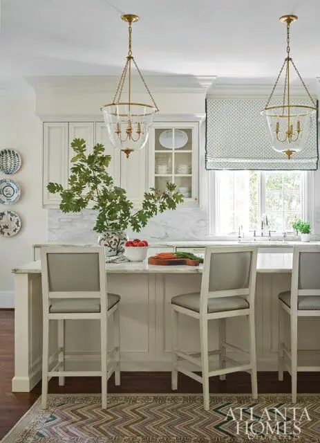 White kitchen island with marble countertop, grey bar stools, and glass pendant lights.