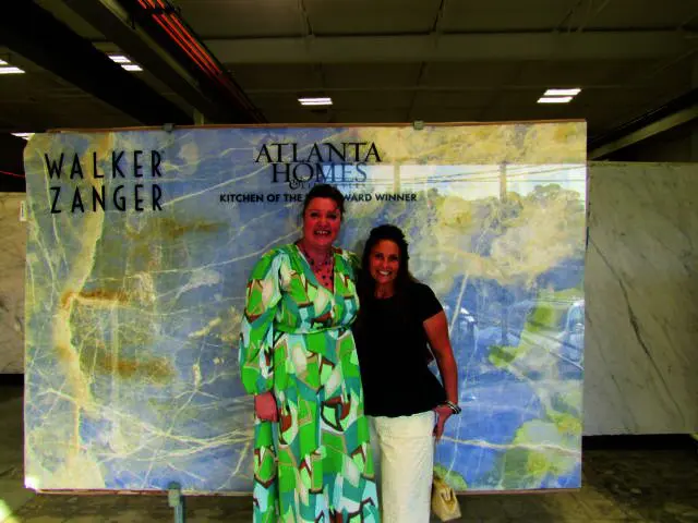 Two women stand in front of a large slab of blue and white marble with gold veining.