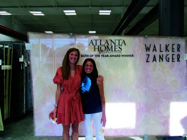 Two women stand in front of a large slab of pink marble with "Atlanta Homes & Lifestyles" and