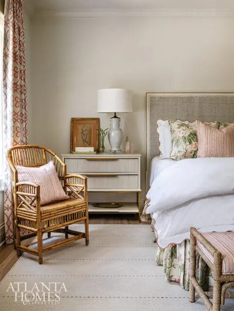 Bedroom with rattan chair, white bedding, floral skirt, and cane headboard. Atlanta Homes &