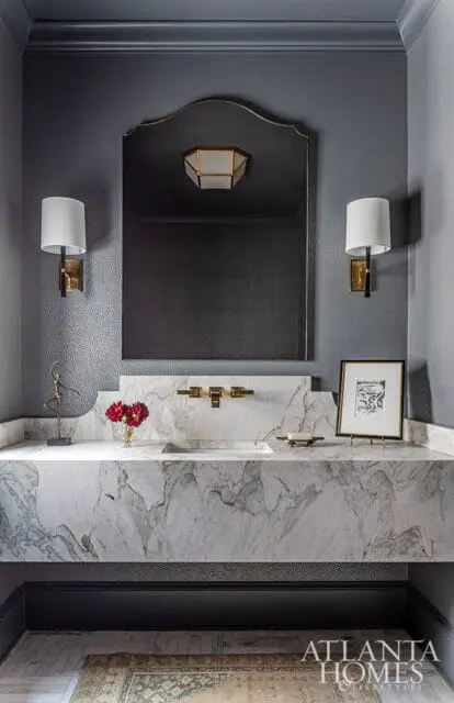 Gray powder room with marble vanity, brass fixtures, sconces, and arched mirror.