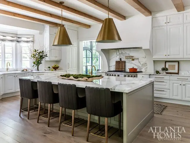 Kitchen with white cabinets, marble island, brass pendant lights, and wood beams