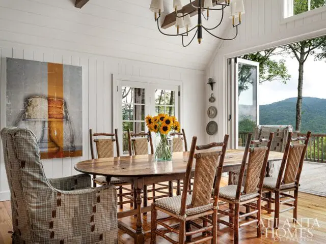 Dining room with oval wooden table, woven chairs, and large windows overlooking mountains