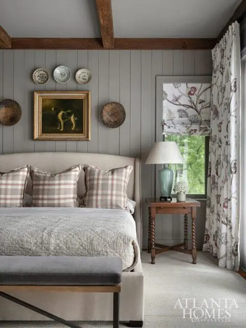 Bedroom with gray paneled walls, plaid pillows, and floral curtains.