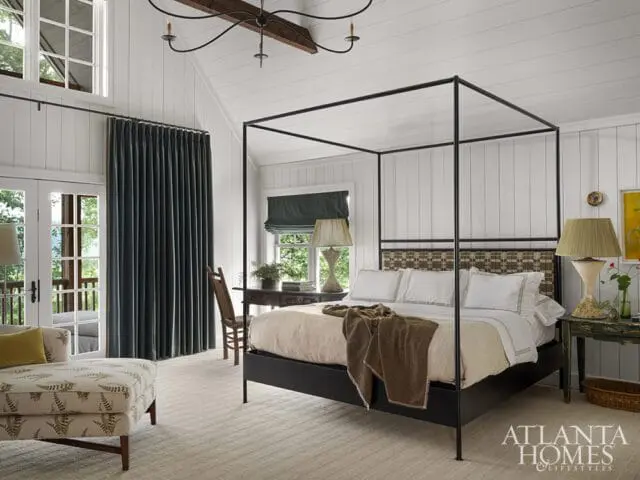 Bedroom with white paneled walls, black canopy bed, and patterned chaise lounge.