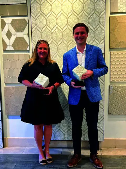 Woman in black dress and man in blue blazer holding awards in front of tile samples