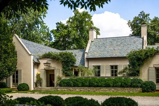 European courtyard house with stucco exterior, slate roof, and lush landscaping.