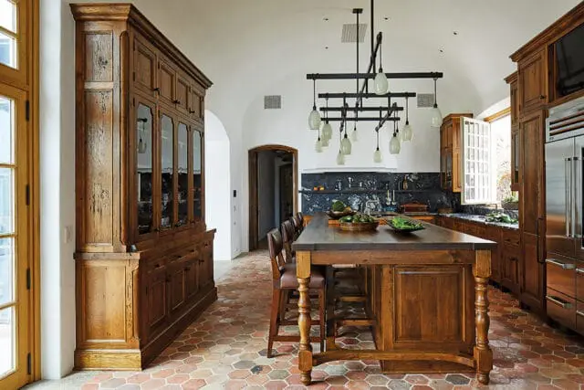 Wooden kitchen with large hutch, island, and marble backsplash. Hexagonal floor tiles.