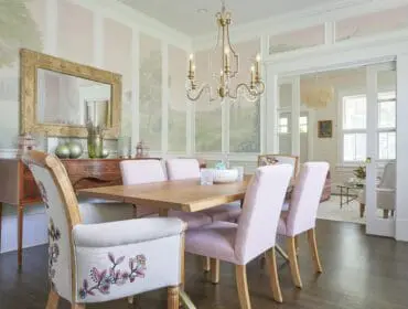 Dining room with pink upholstered chairs, wooden table, and scenic wallpaper.