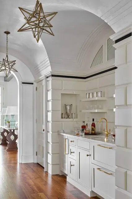 White bar area with marble countertop, brass faucet, and starburst pendant lights.