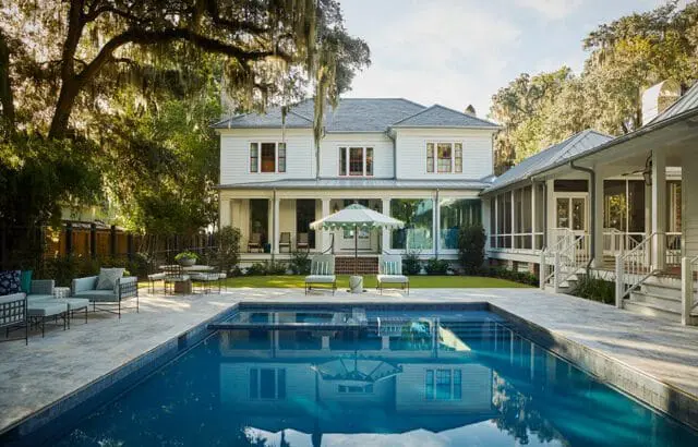 White house with wraparound porch and pool, surrounded by trees with Spanish moss.