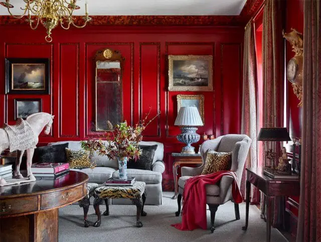 Red paneled living room with gray sofa, armchair, and ornate chandelier.