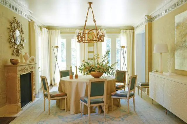 Dining room with a round table, floral centerpiece, ornate chandelier, and fireplace.