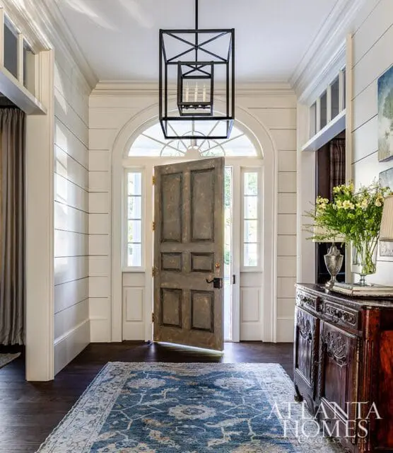 Entryway with arched doorway, distressed gray door, blue patterned rug, and dark wood console table.