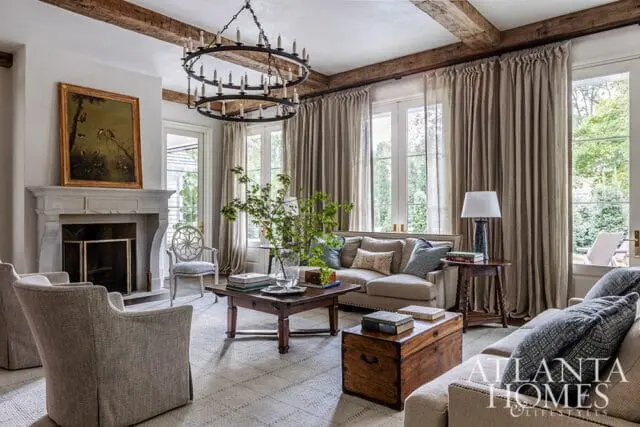 Living room with stone fireplace, exposed beams, neutral sofa, and wooden trunk